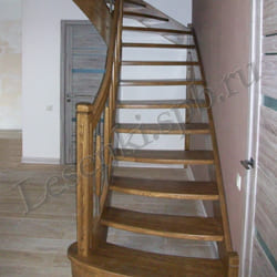 Фотография лестницы с поворотом на 90 градусов из массива дуба с гнутой тетивой и перилом. Покрытие – бесцветный лак
